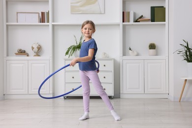 Cute little girl exercising with hula hoop indoors