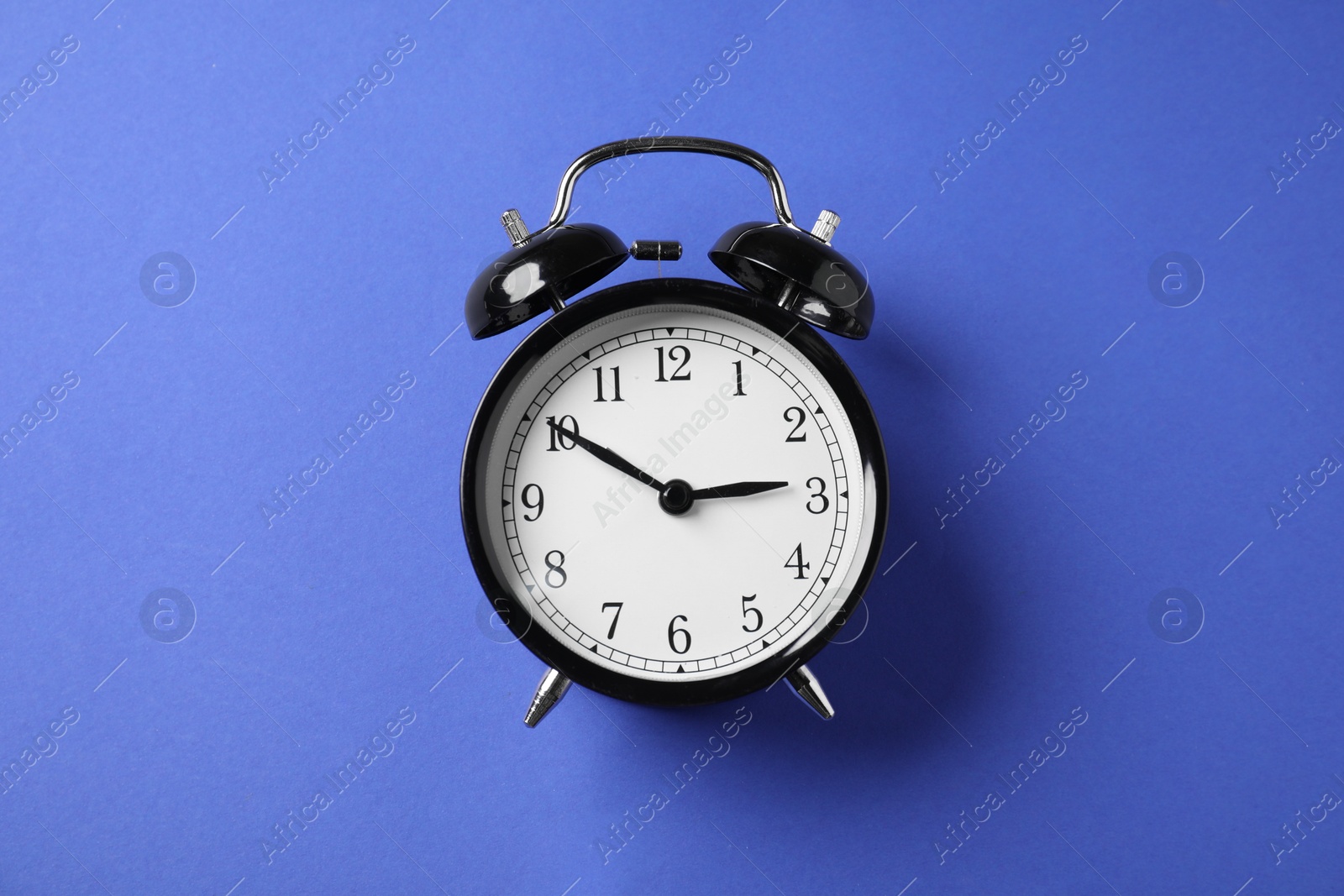 Photo of One black alarm clock on blue background, top view