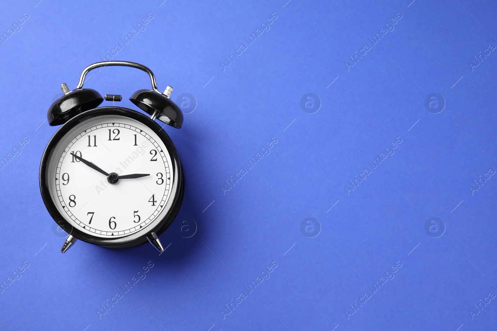 Photo of One black alarm clock on blue background, top view. Space for text