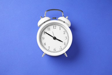 One white alarm clock on blue background, top view