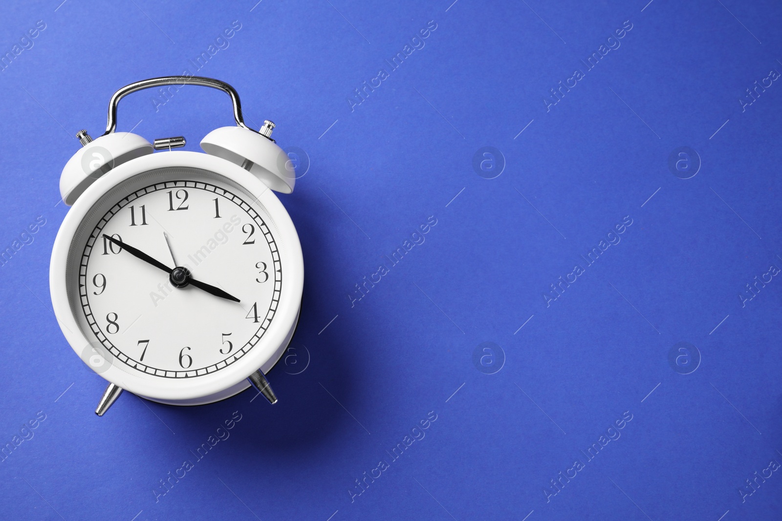 Photo of One white alarm clock on blue background, top view. Space for text