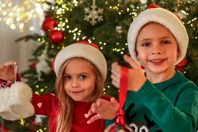 Photo of Little kids in Santa hats with Christmas ornaments at home