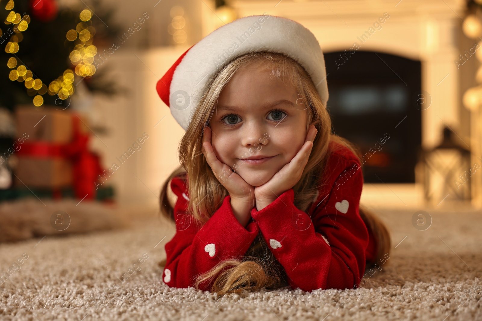 Photo of Little girl in Santa hat on floor at home. Christmas celebration