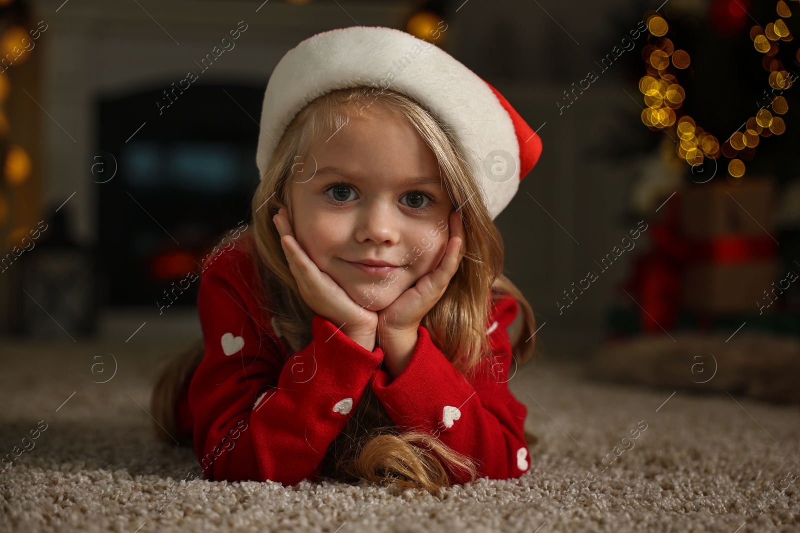 Photo of Little girl in Santa hat on floor at home. Christmas celebration