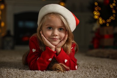 Photo of Little girl in Santa hat on floor at home. Christmas celebration