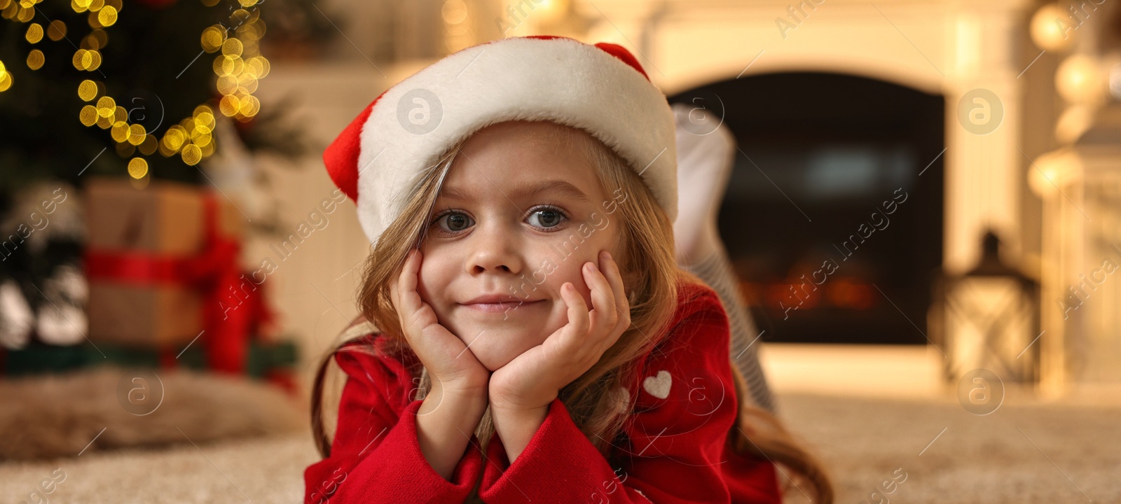 Photo of Little girl in Santa hat on floor at home. Christmas celebration