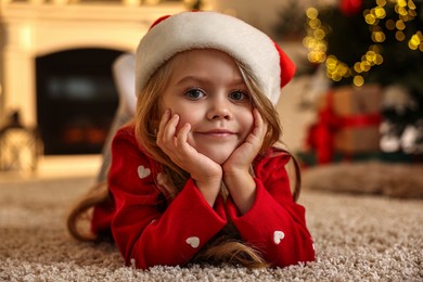 Photo of Little girl in Santa hat on floor at home. Christmas celebration