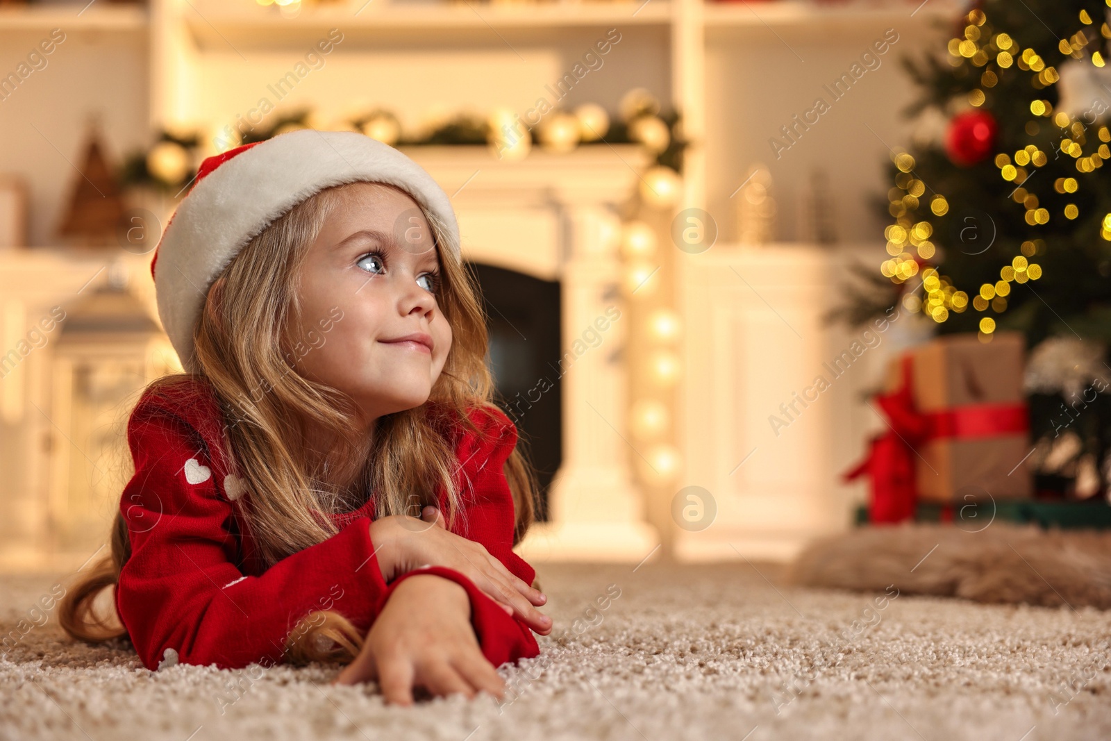 Photo of Little girl in Santa hat on floor at home, space for text. Christmas celebration