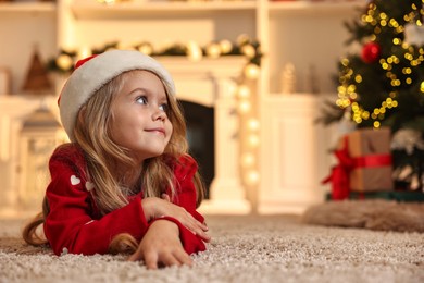 Little girl in Santa hat on floor at home, space for text. Christmas celebration