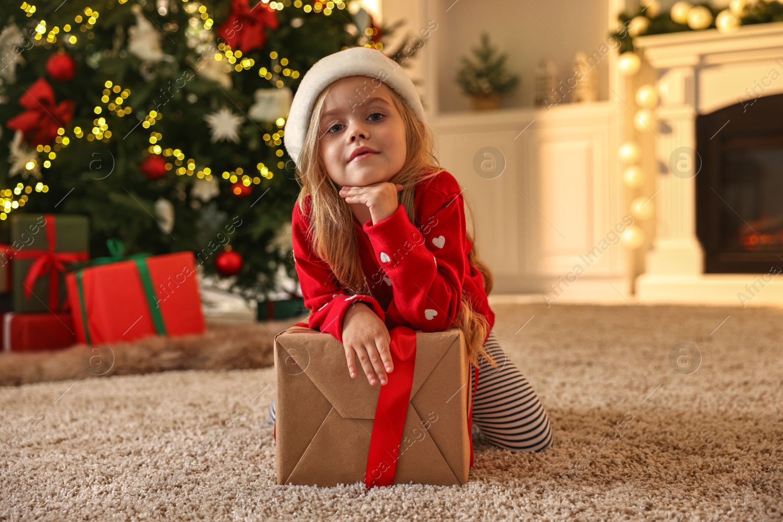 Photo of Little girl in Santa hat with Christmas box at home