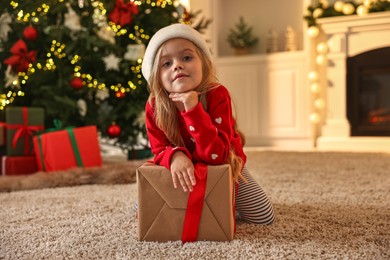 Little girl in Santa hat with Christmas box at home