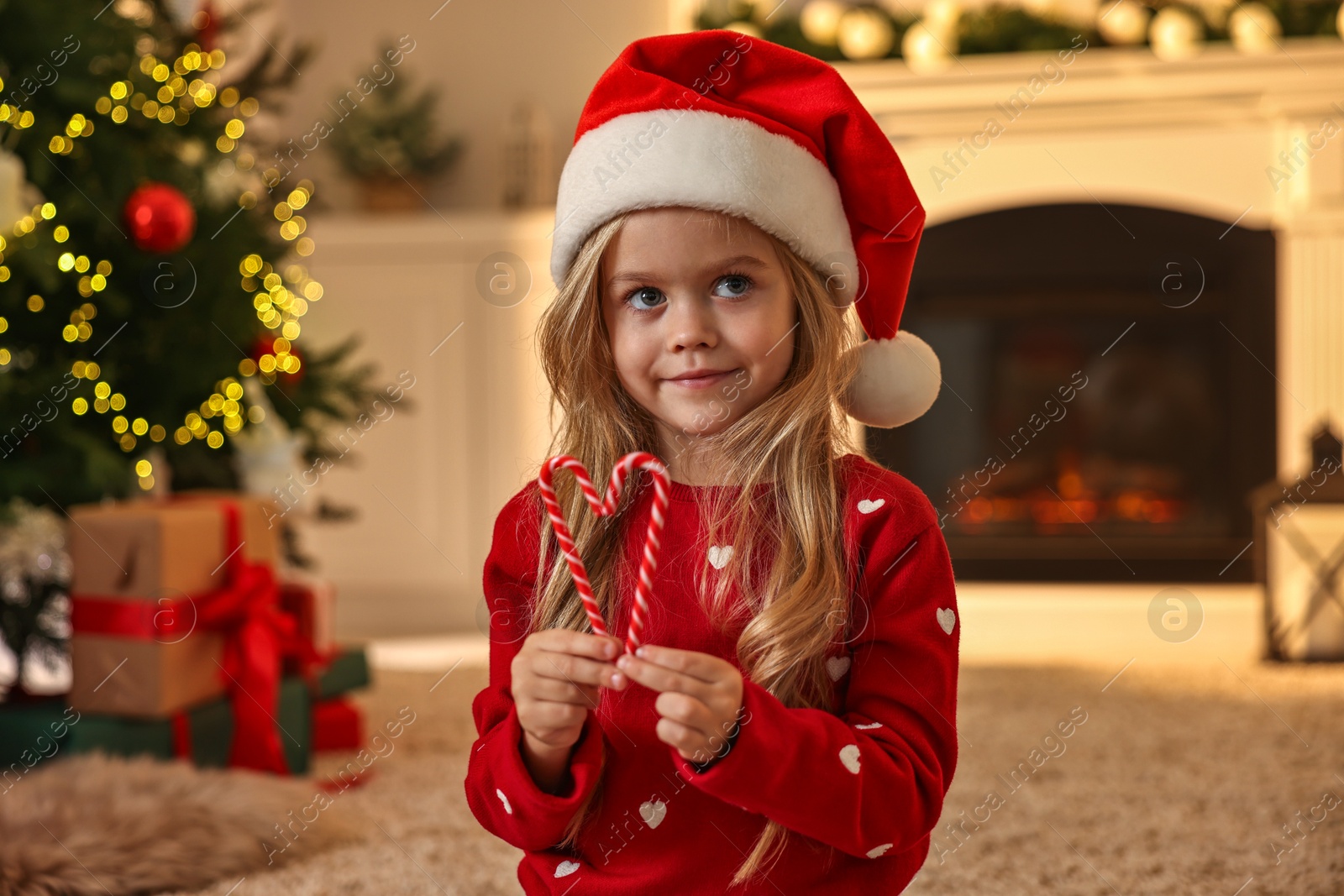 Photo of Little girl in Santa hat with candy canes at home. Christmas celebration