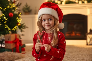 Little girl in Santa hat with candy canes at home. Christmas celebration