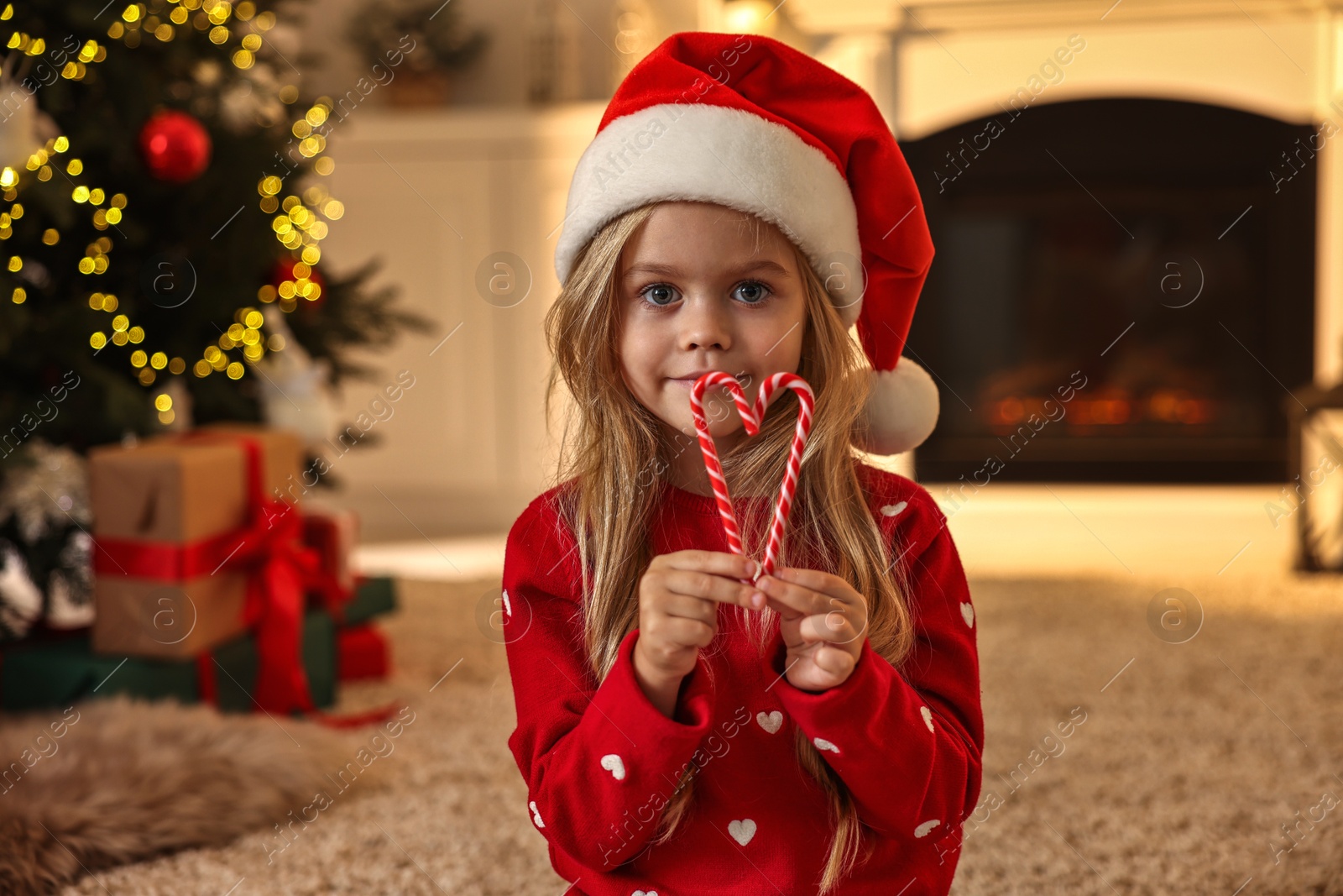 Photo of Little girl in Santa hat with candy canes at home. Christmas celebration