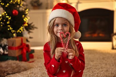 Photo of Little girl in Santa hat with candy canes at home. Christmas celebration