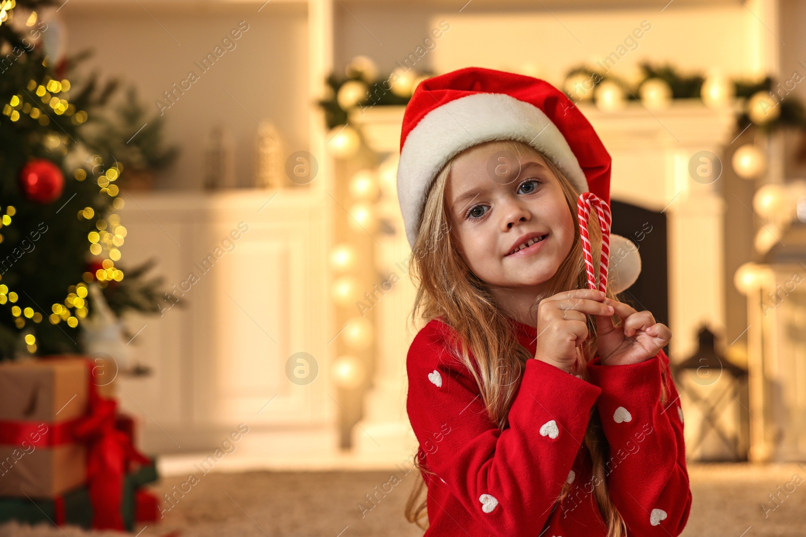 Photo of Little girl in Santa hat with candy canes at home, space for text. Christmas celebration