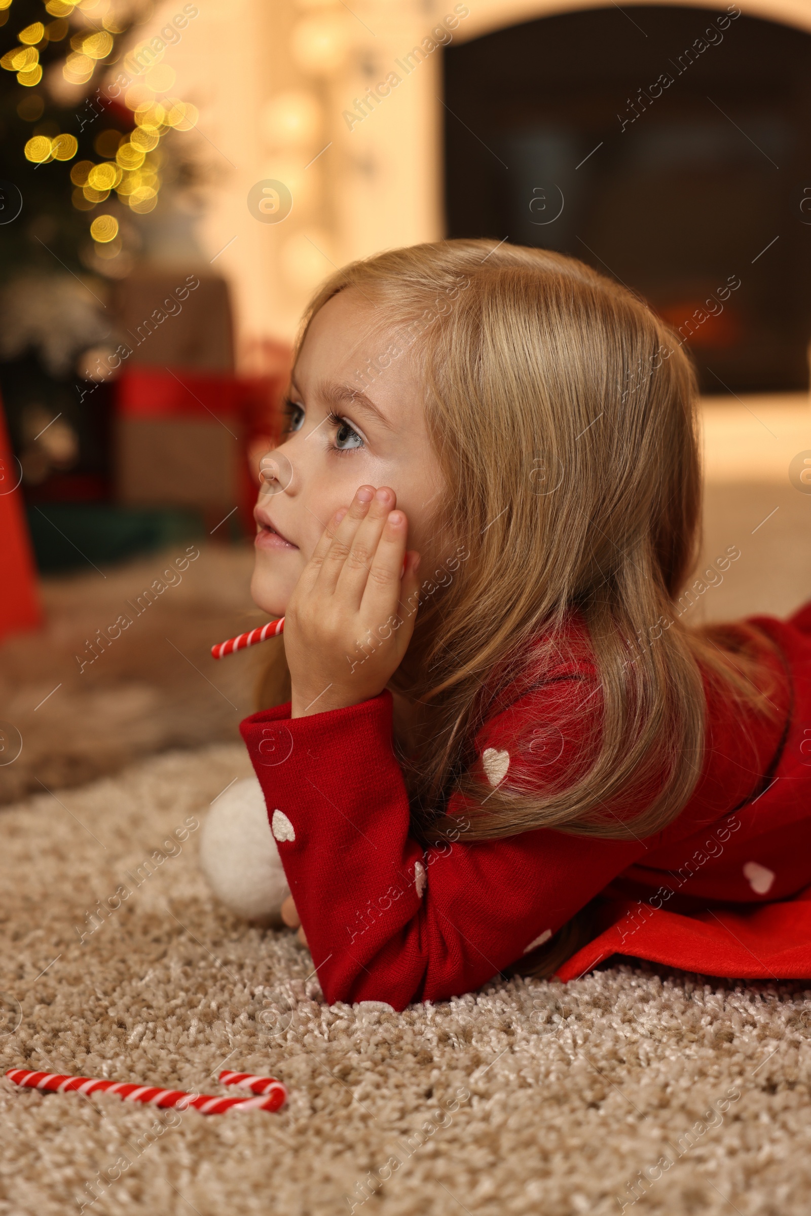 Photo of Little girl with candy canes on floor at home. Christmas celebration