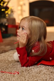 Photo of Little girl with candy canes on floor at home. Christmas celebration