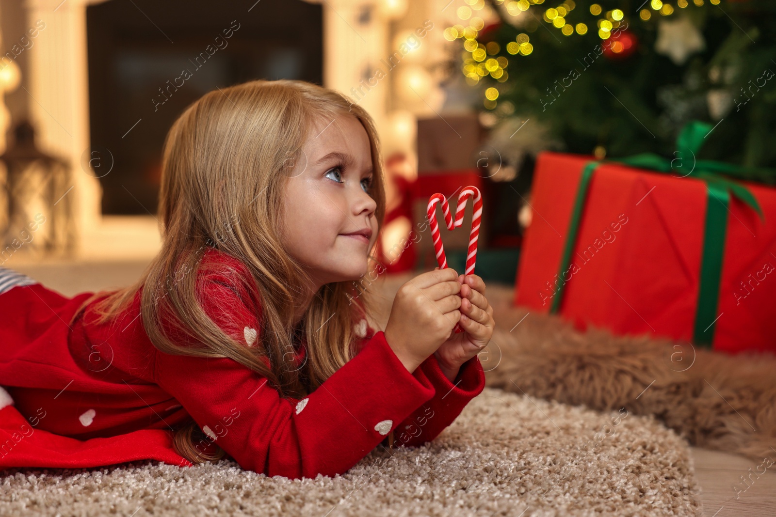 Photo of Little girl with candy canes on floor at home. Christmas celebration