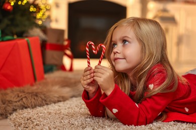 Little girl with candy canes on floor at home. Christmas celebration