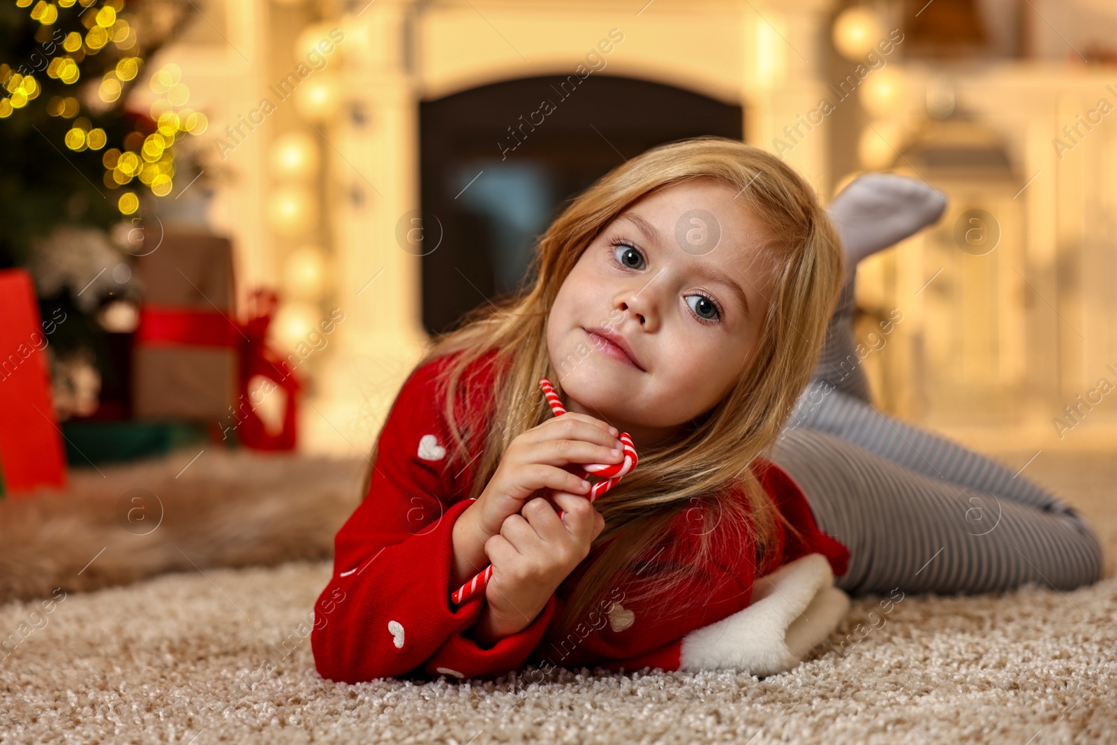 Photo of Little girl with candy canes on floor at home. Christmas celebration