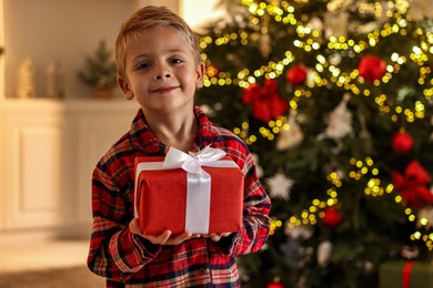 Little boy with Christmas box at home, space for text