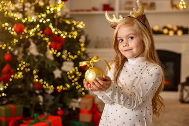 Photo of Little girl with Christmas ornament at home, space for text