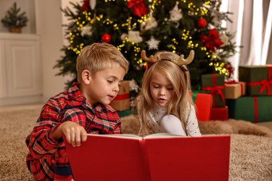 Photo of Little kids reading book on floor at home. Christmas celebration