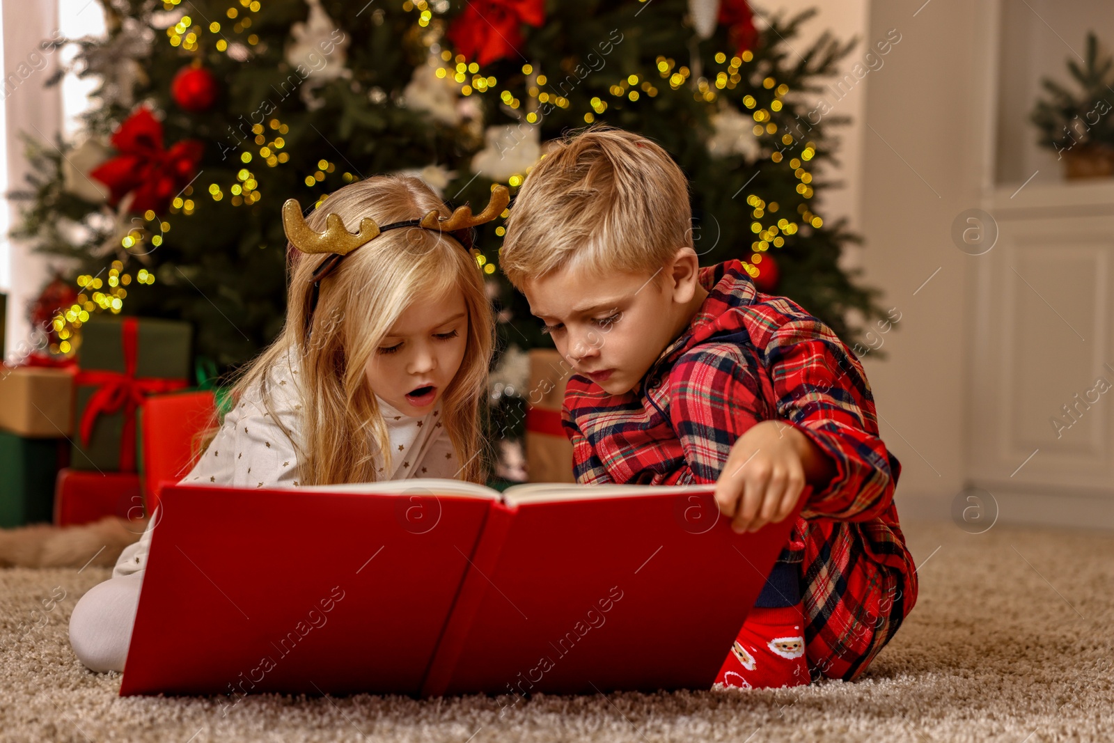 Photo of Little kids reading book on floor at home. Christmas celebration