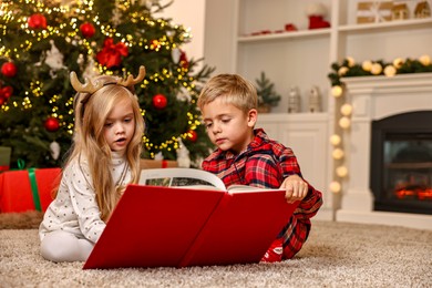 Little kids reading book on floor at home. Christmas celebration