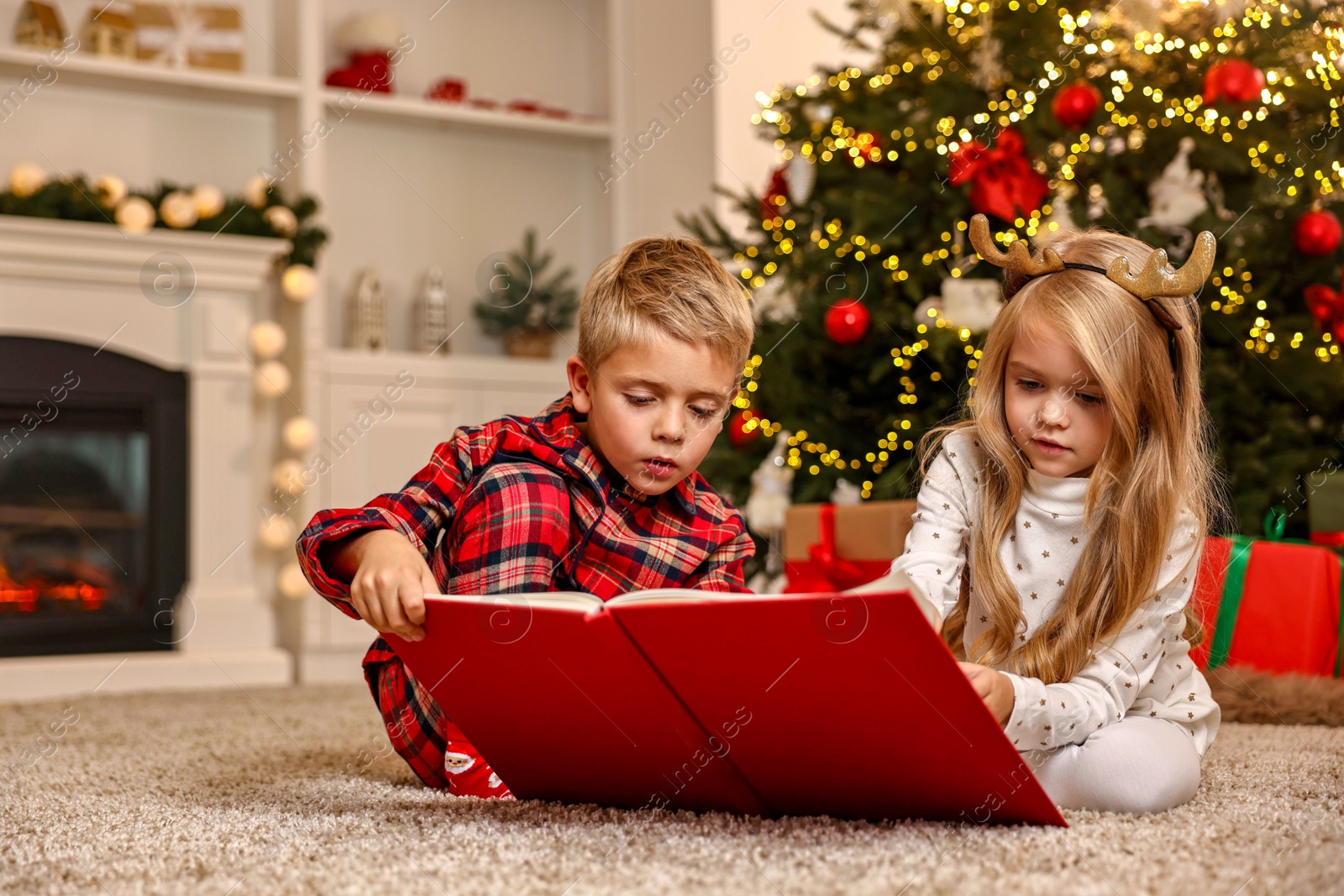 Photo of Little kids reading book on floor at home. Christmas celebration