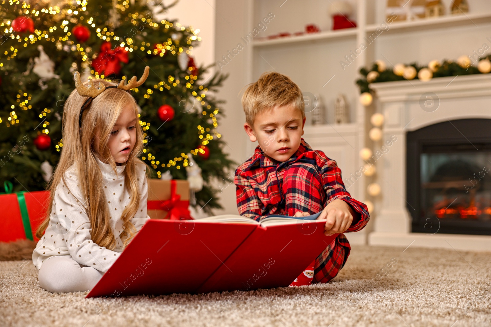 Photo of Little kids reading book on floor at home. Christmas celebration