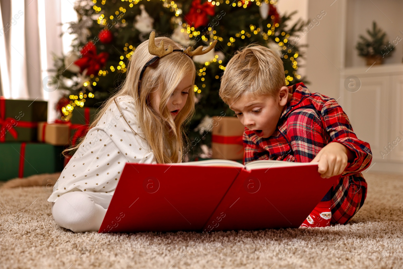 Photo of Little kids reading book on floor at home. Christmas celebration