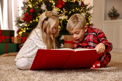 Photo of Little kids reading book on floor at home. Christmas celebration