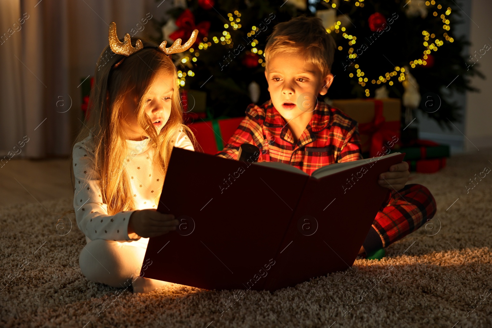 Photo of Little kids reading book on floor at home. Christmas celebration