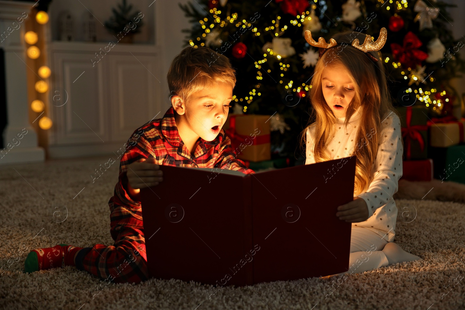 Photo of Little kids reading book on floor at home. Christmas celebration