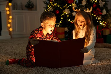 Photo of Little kids reading book on floor at home. Christmas celebration