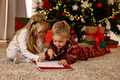 Photo of Little kids writing letter to Santa Claus on floor at home. Christmas celebration