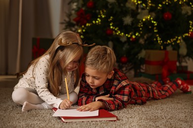 Photo of Little kids writing letter to Santa Claus on floor at home. Christmas celebration