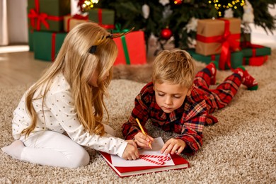 Little kids writing letter to Santa Claus on floor at home. Christmas celebration