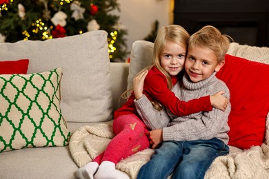 Photo of Little kids hugging on sofa in room decorated for Christmas