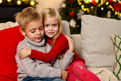 Photo of Little kids hugging on sofa in room decorated for Christmas