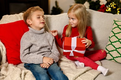 Photo of Little kids with Christmas gift on sofa at home