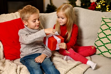 Photo of Little kids with Christmas gift on sofa at home