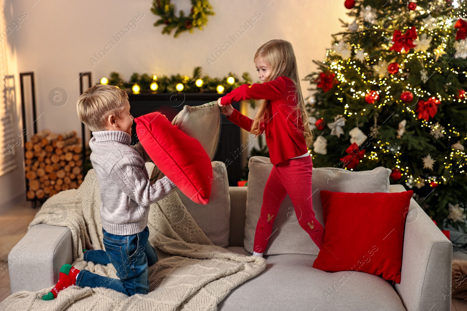 Photo of Little kids having pillow fight on sofa in room decorated for Christmas