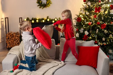 Little kids having pillow fight on sofa in room decorated for Christmas