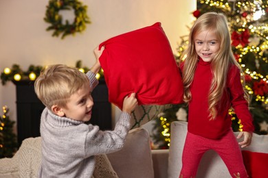 Photo of Little kids having pillow fight on sofa in room decorated for Christmas