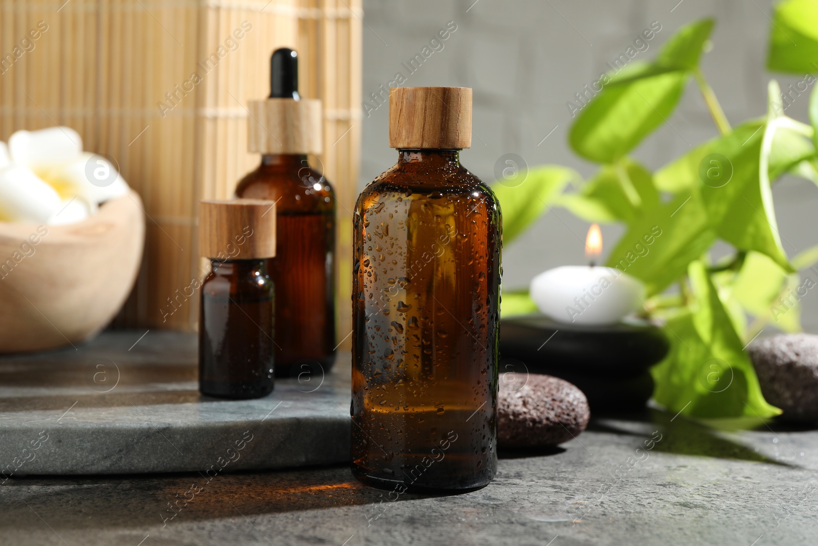 Photo of Spa composition with cosmetic products and burning candle on grey table, closeup