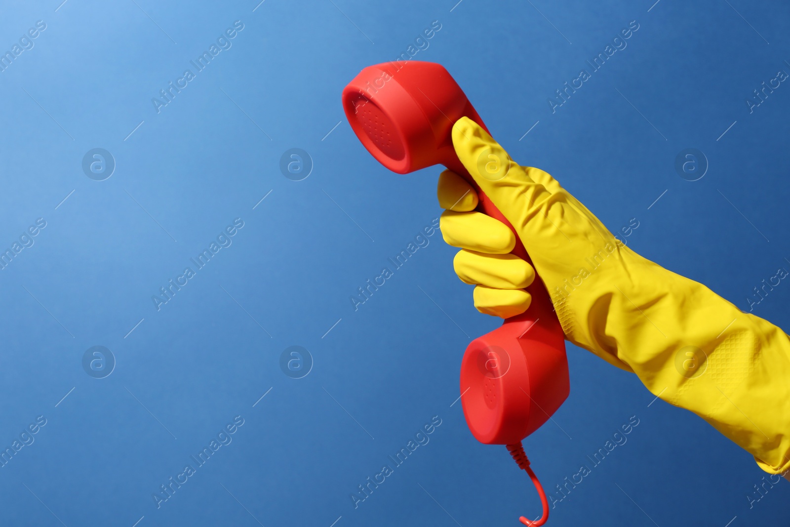 Photo of Woman in rubber glove holding red telephone handset on blue background, closeup. Space for text