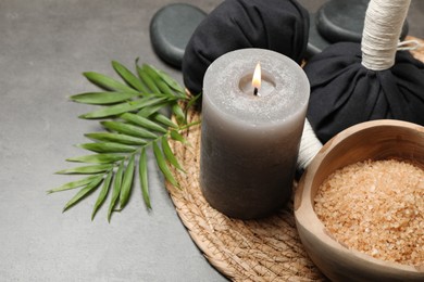 Photo of Spa composition with herbal bags and burning candle on grey table, closeup